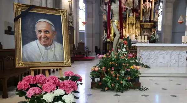 Obraz ojca świętego Franciszka w kościele, otoczony kwiatami i krzyżem.
